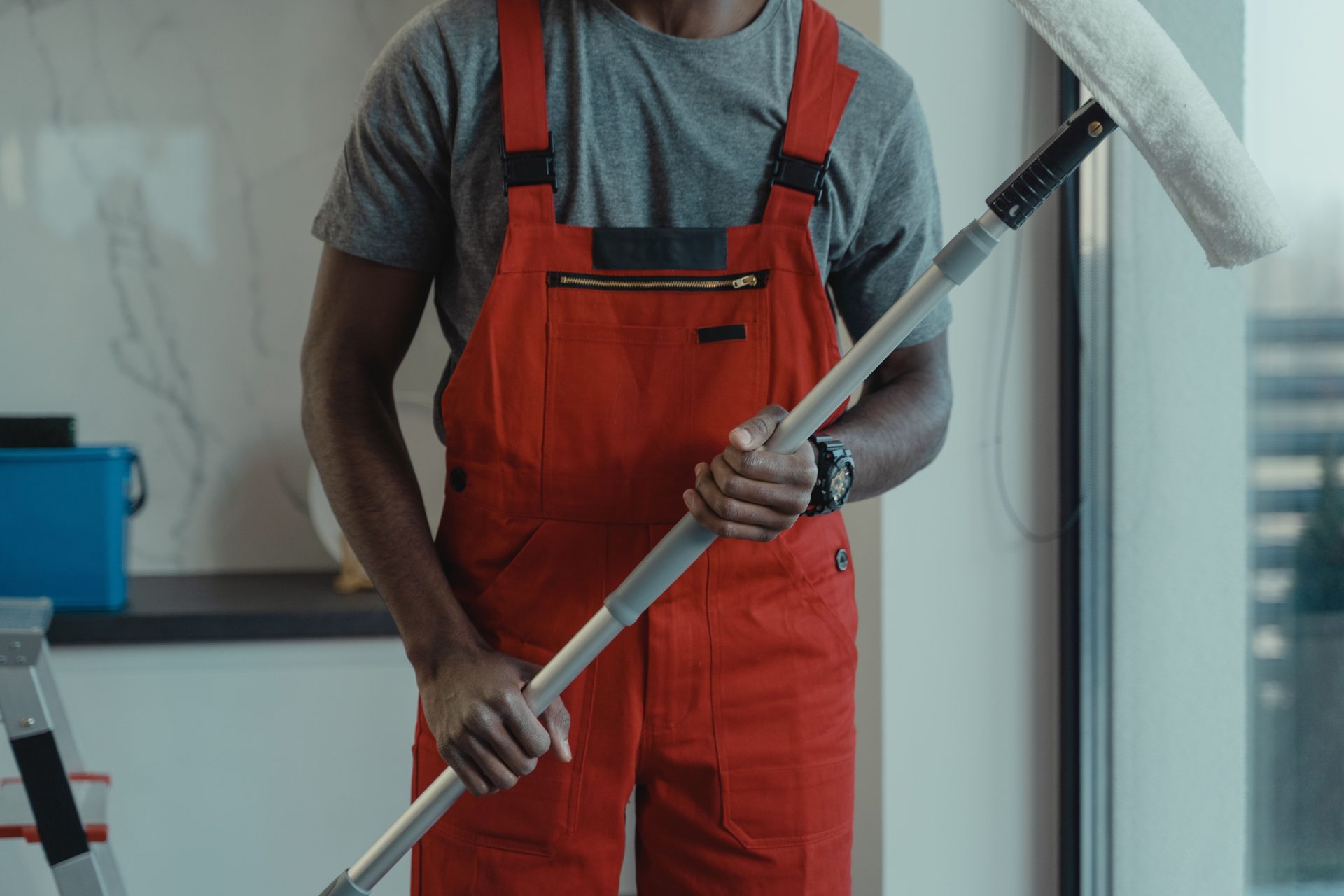 Eine professionelle Reinigungskraft in rotem Overall hält einen Wischmopp, während sie Innenräume reinigt.