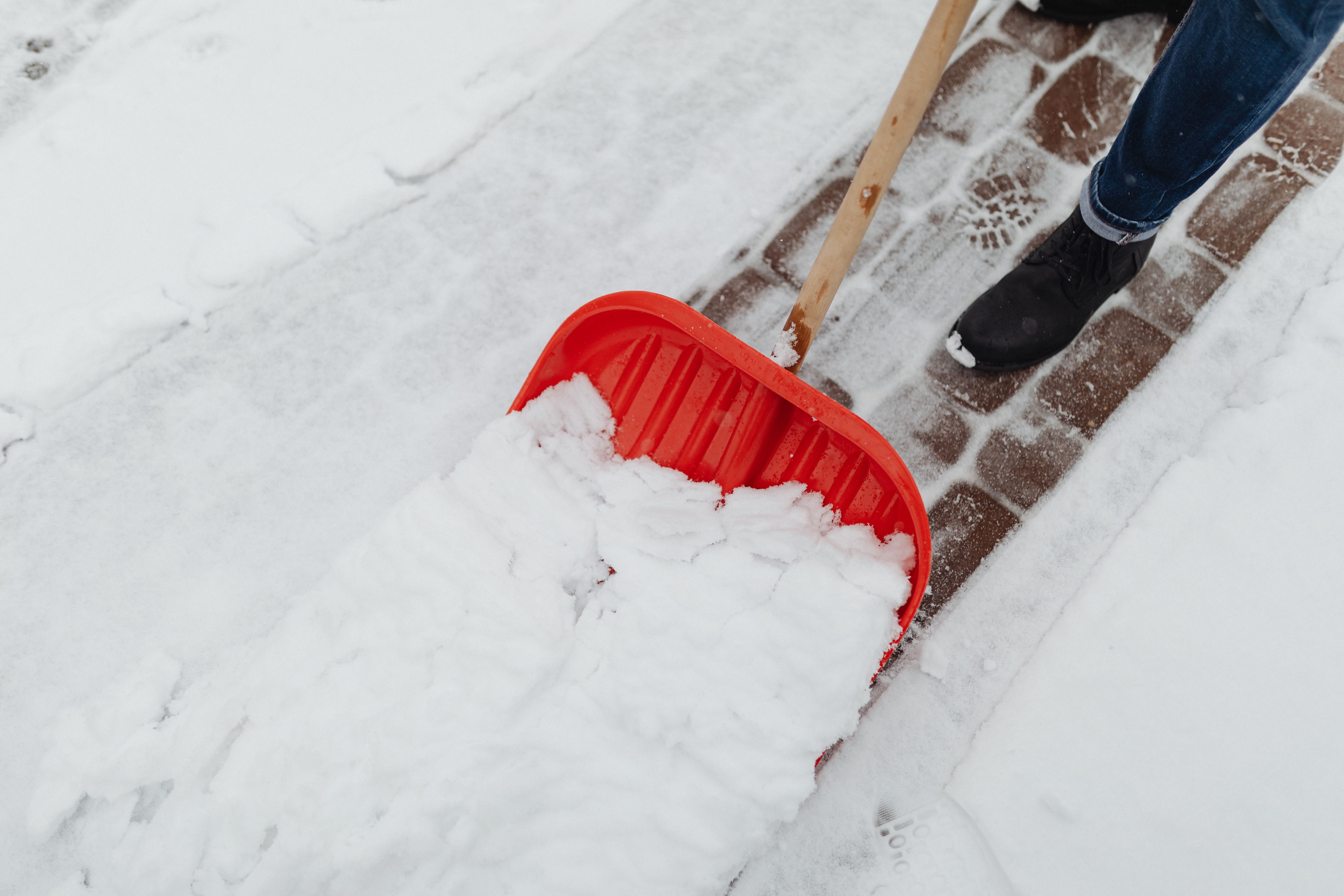 Ein erwachsener Mann schippt an einem kalten Wintertag Schnee – eine typische Aktivität bei winterlichem Wetter.